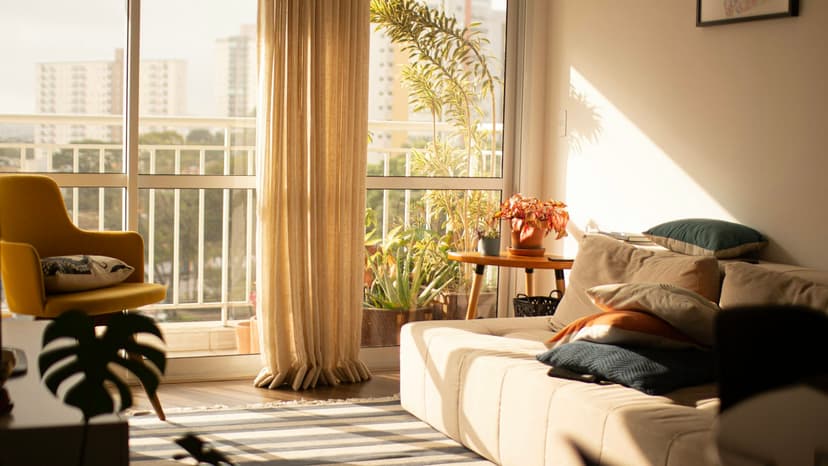 Sonnendurchflutetes Wohnzimmer einer Mietwohnung mit Sofa, Vorhang und Blick auf den Balkon