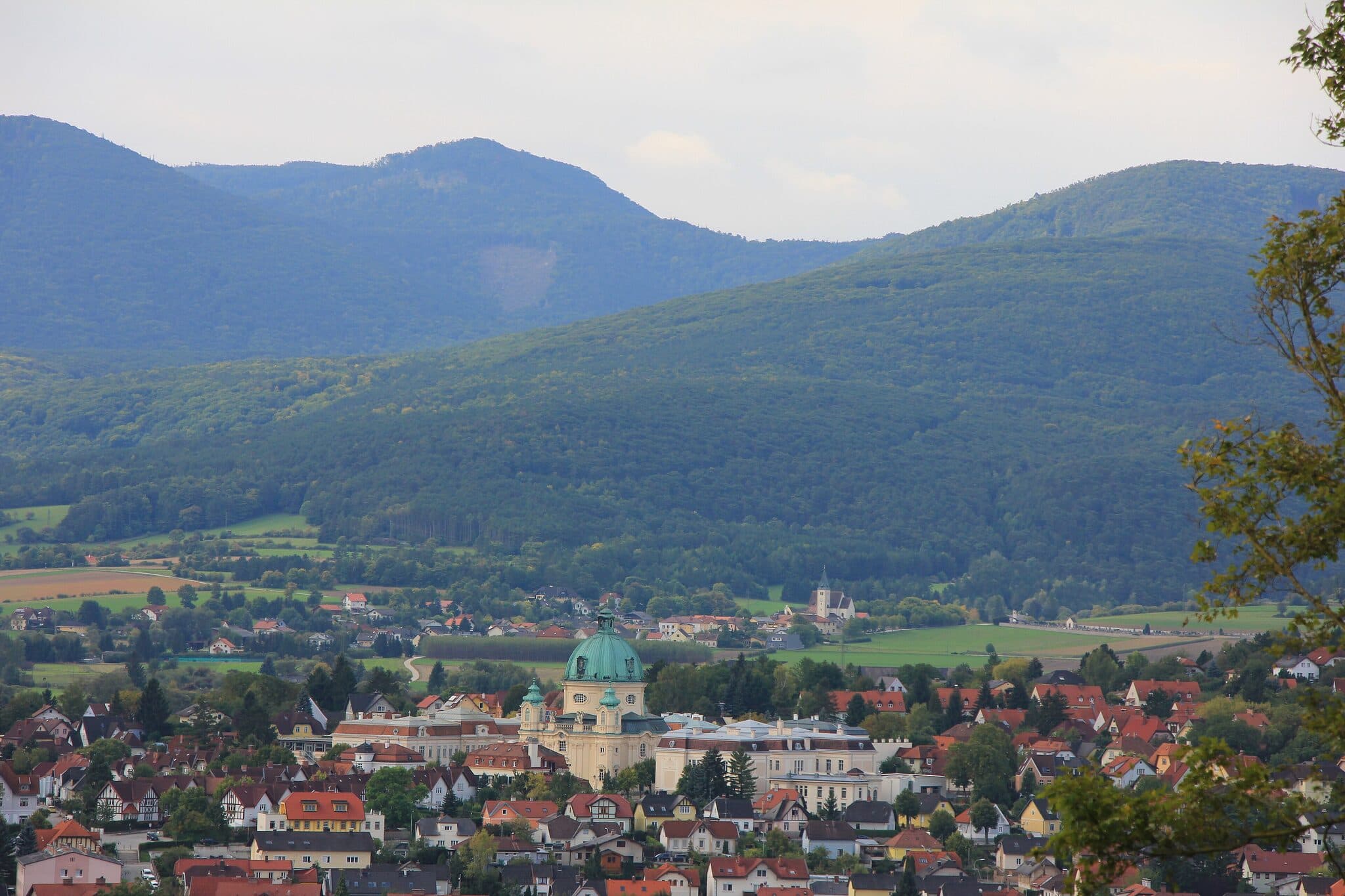 Panorama-Ortsansicht von Berndorf: Ort im Tal mit roten Daechern und bewaldeter Bergkulisse im Hintergrund