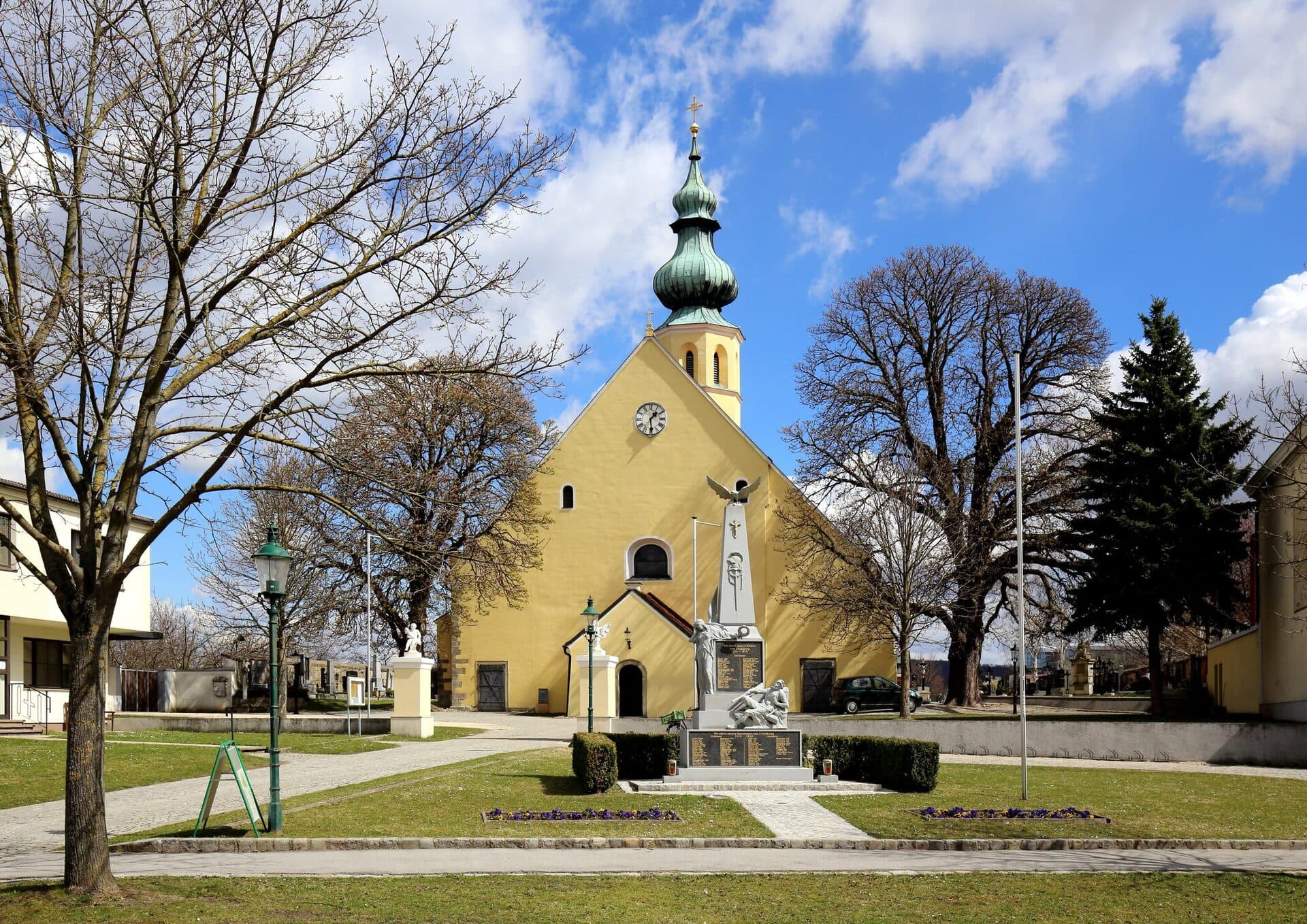 Pfarrkirche in Rückersdorf, einer Katastralgemeinde der Gemeinde Harmannsdorf: gelbe Kirche mit Zwiebelturm vor blauem Himmel, gut belichtet