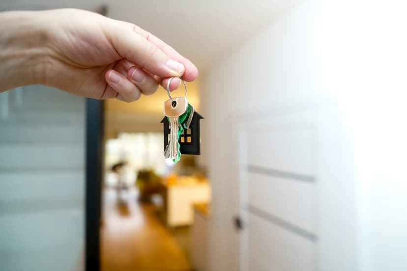 Hand hält einen Schlüsselbund mit Haus-Anhänger in einer hellen Wohnung