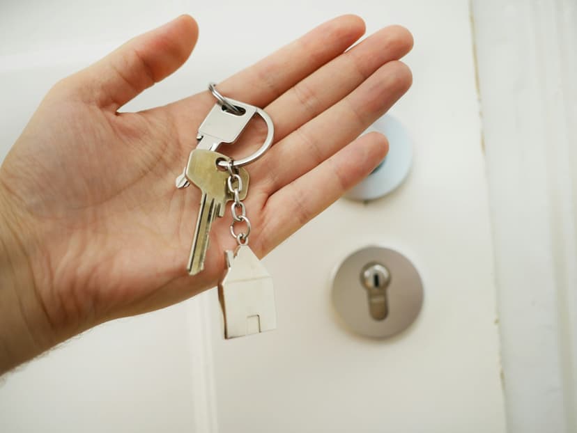 Offene Hand mit Wohnungsschlüssel und Haus-Anhänger vor einer weißen Wohnungstür